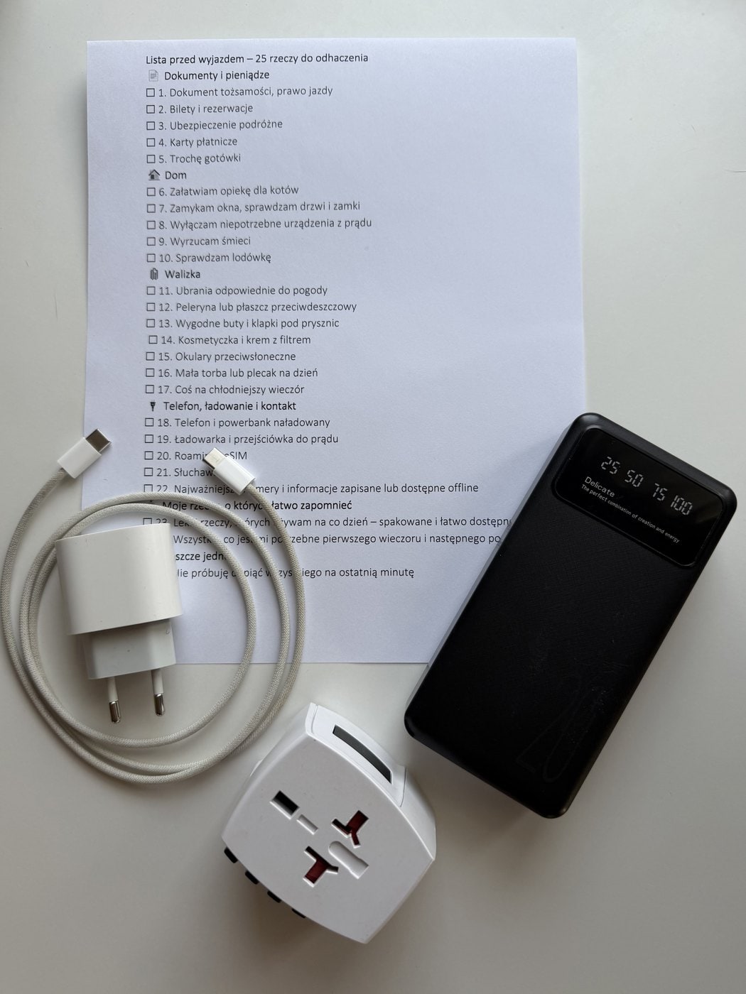 Wydrukowana lista przed wyjazdem, obok powerbank, ładowarka i uniwersalna przejściówka do gniazdek