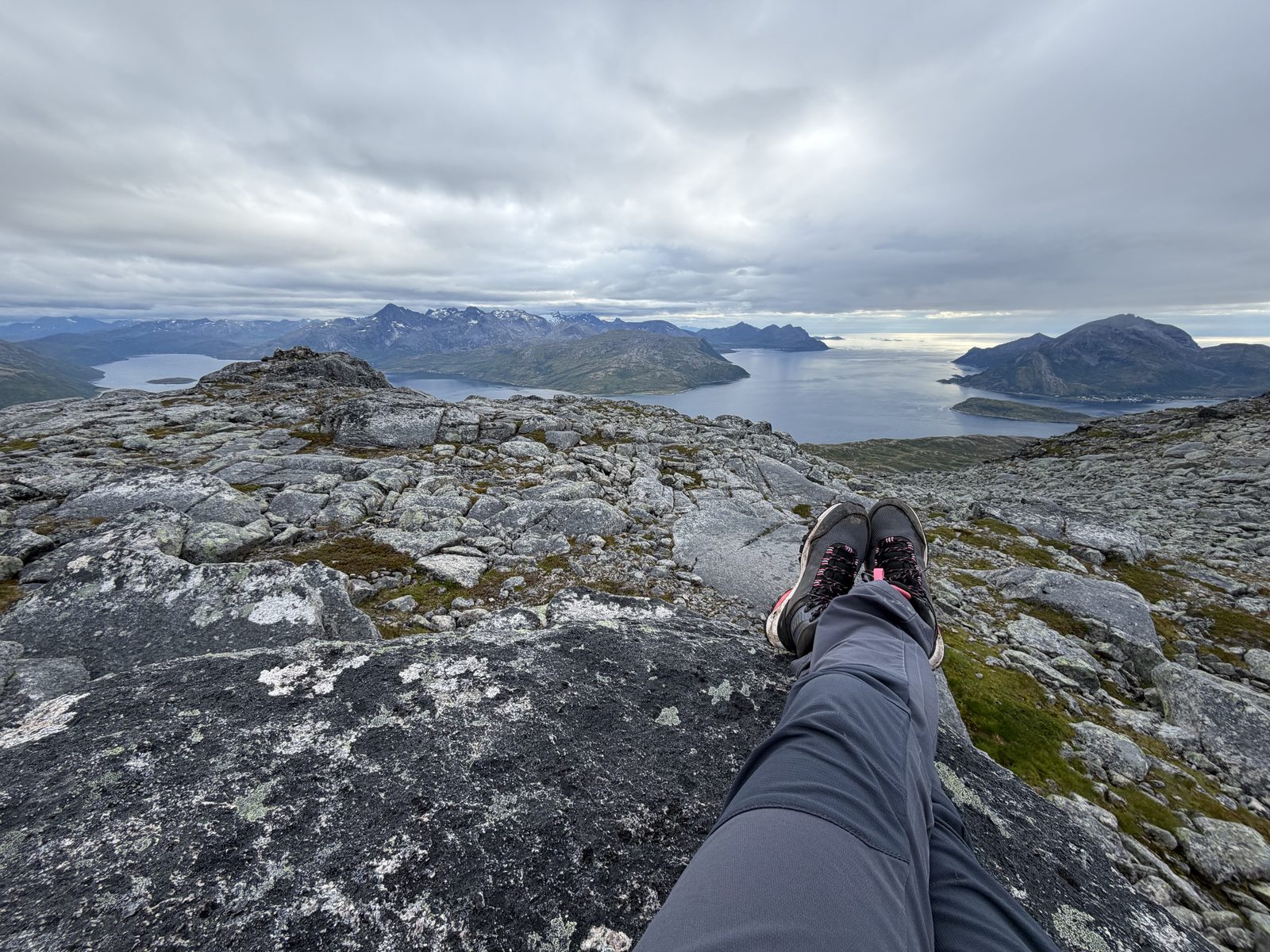 Nogi wyciągnięte na skale, w dole fiord i góry — przerwa w połowie szlaku